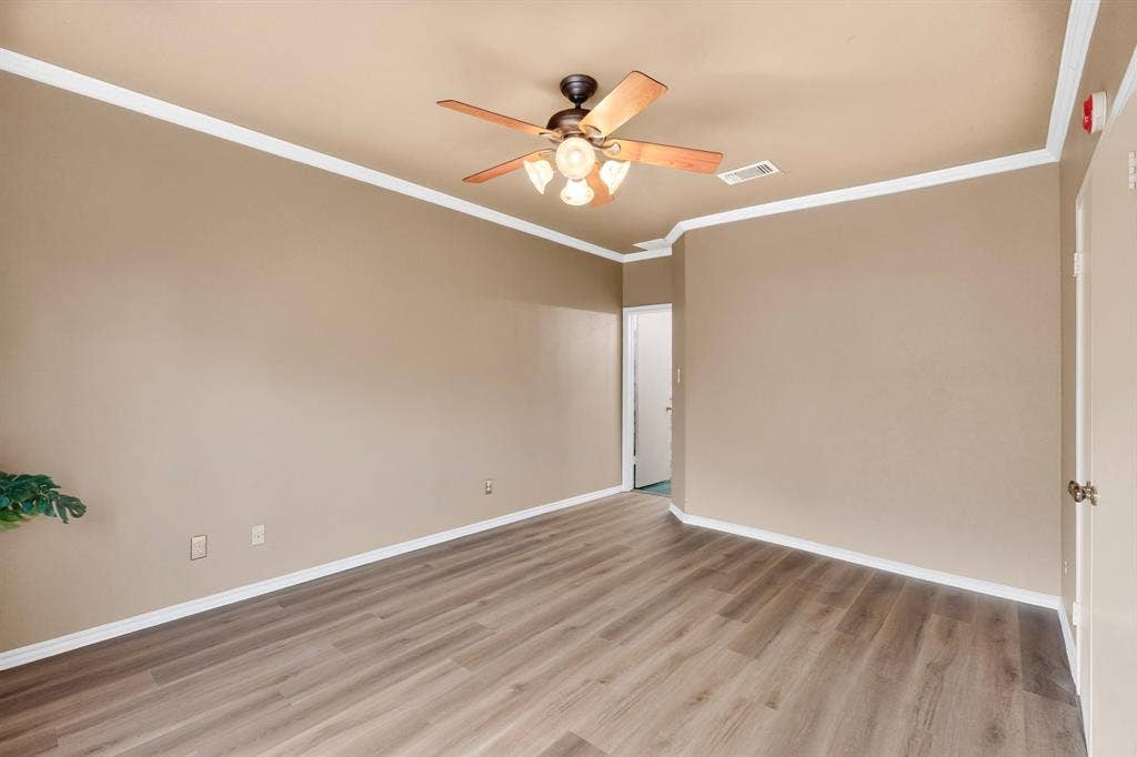 Primary bedroom features newly installed wood-finish flooring, neutral wall paint, crown molding, and a ceiling fan with integrated lighting.