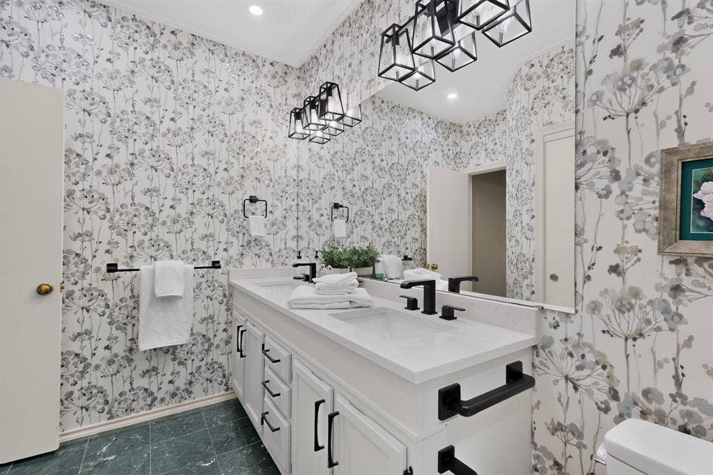 Double vanity with white cabinetry, stone-finish countertops, and matte black hardware create a modern finish in this updated ensuite primary bathroom.
