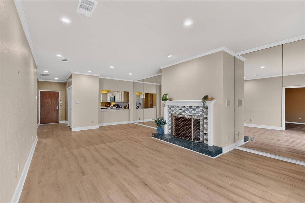 Blank slate of a living area — ready for your personal touches — featuring wood-finish flooring, recessed lighting, floor-to-ceiling mirrored walls, and a fireplace with decorative tile surround and hearth.