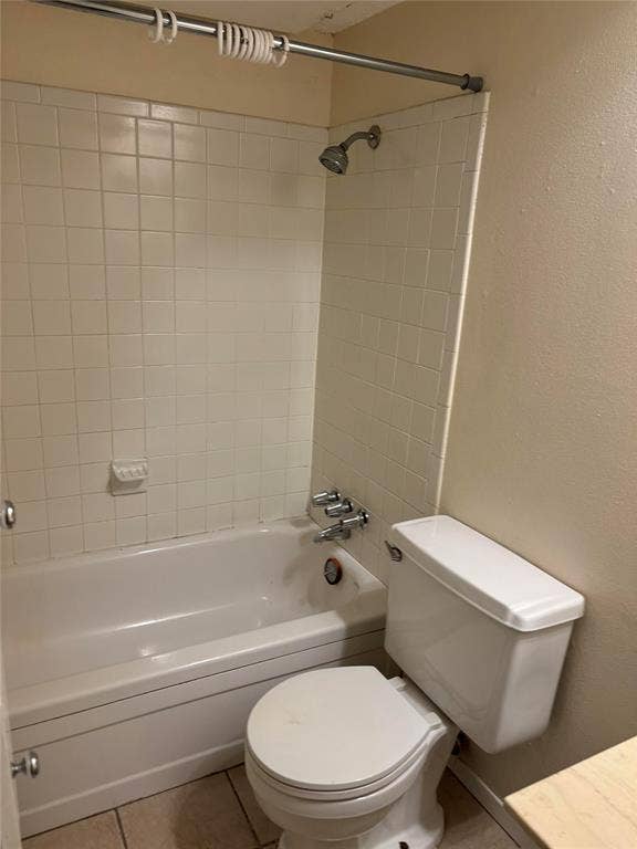Bathroom with tile floors, toilet, and tiled shower / bath combo