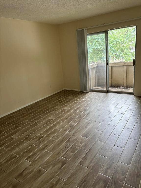 Empty room with dark hardwood / wood-style floors and a textured ceiling