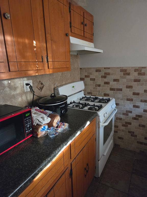 Kitchen featuring stained wood cabinetry, stone-texture countertops, a tiled backsplash, and an integrated range hood