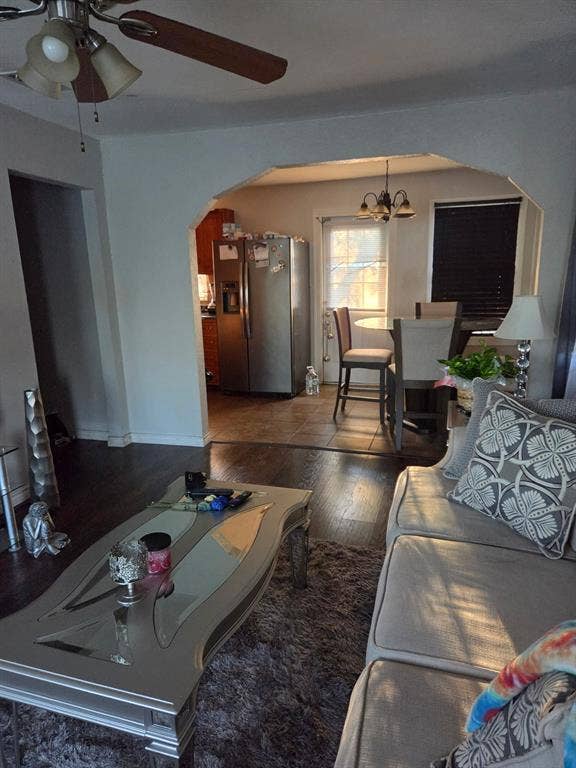 Interior featuring wood-finish flooring, a decorative arched wall opening, a stainless-steel refrigerator, tile flooring, and a ceiling fan with integrated lighting