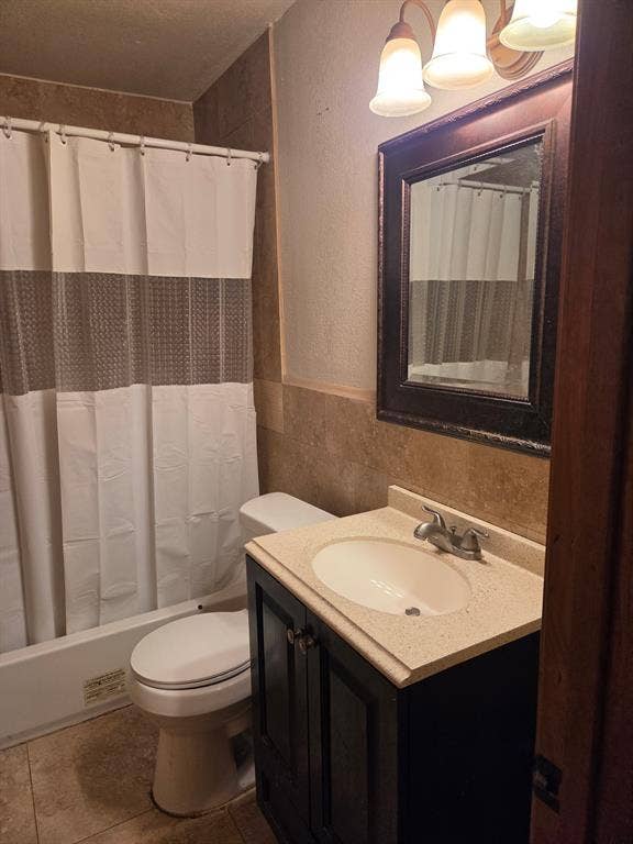 Bathroom featuring a dark-finish vanity with a stone-composite countertop, an integrated sink with a dual-handle faucet, neutral tile flooring, and tile wainscoting