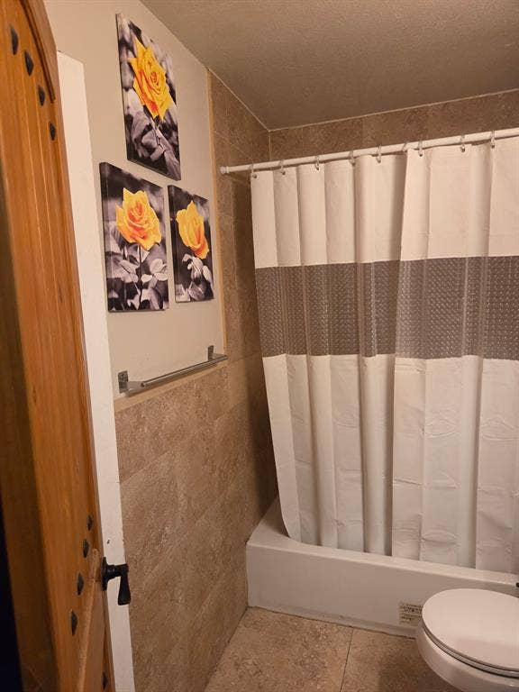 Bathroom featuring tan wall-to-wall ceramic tile surround, a standard-size soaking tub, and a metal towel bar