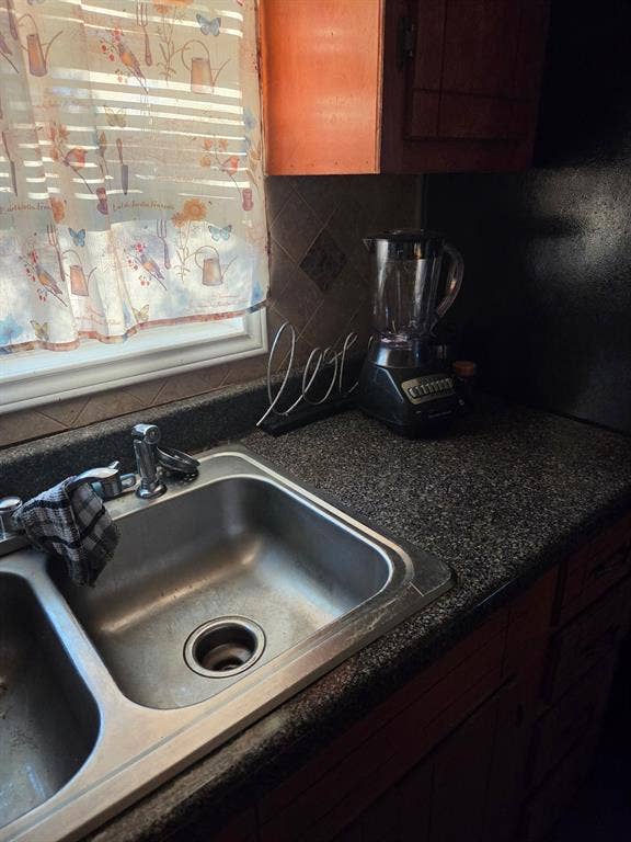 Kitchen featuring a dual-basin stainless steel sink, stone-finish countertops, tiled backsplash, and wood-finish cabinetry