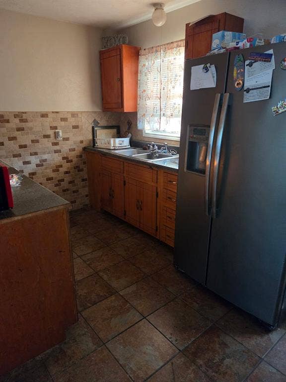 Kitchen featuring wood cabinetry, stone-texture wall tiling, large-format floor tiling, and a stainless steel refrigerator