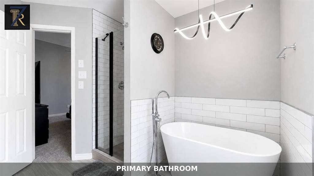 Freestanding soaking tub with a chrome floor-mounted faucet, walk-in shower with black-framed glass enclosure, and white subway tile surrounds