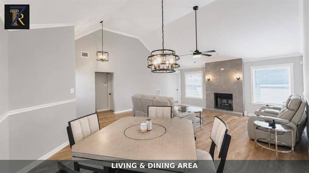 Vaulted ceilings, wood-finish flooring, stone-surround fireplace, and decorative metal pendant lighting