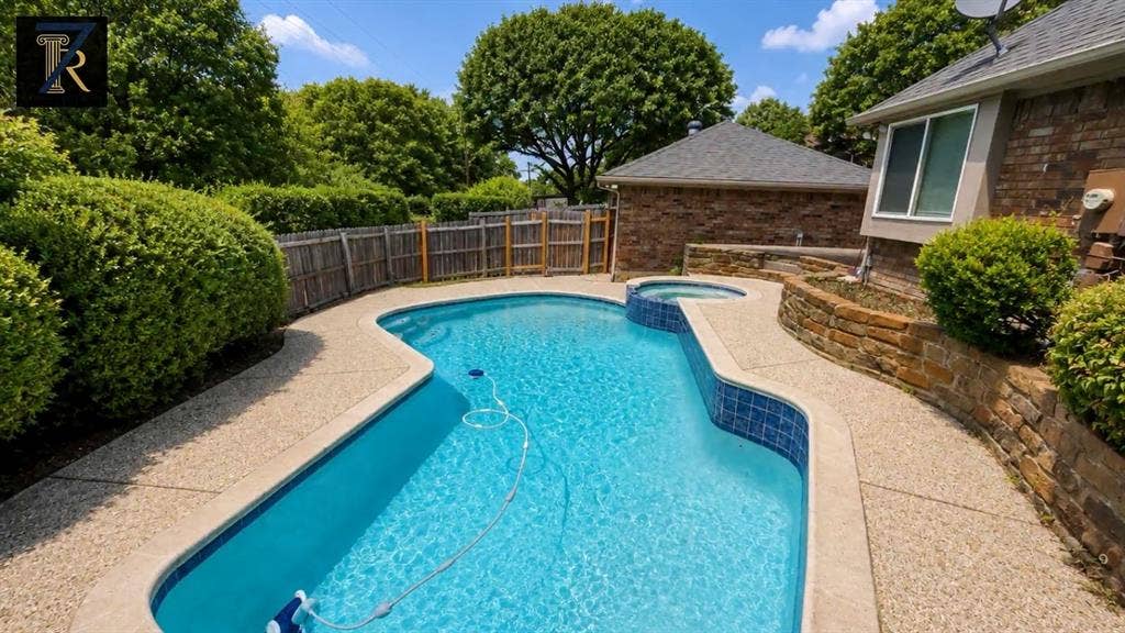 In-ground pool with integrated spa, aggregate concrete decking, stacked stone retaining wall, and wood privacy fencing
