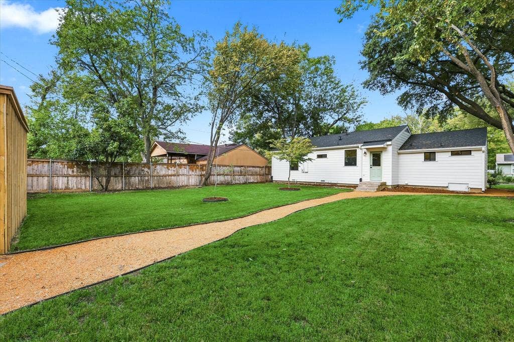 11624 Rupley Lane, Dallas, TX 75218 Expansive backyard featuring a manicured lawn, gravel pathway, wood privacy fencing, and mature trees