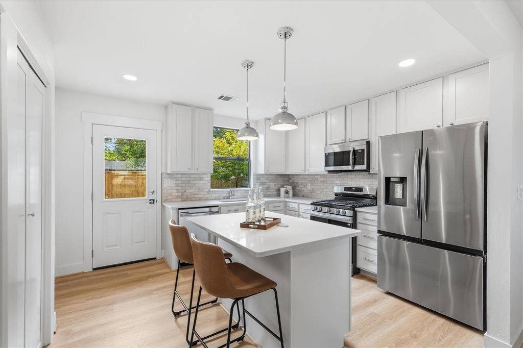 11624 Rupley Lane, Dallas, TX 75218 Kitchen featuring white shaker-style cabinetry, quartz countertops, a central island, stainless steel appliances, and wood-finish flooring