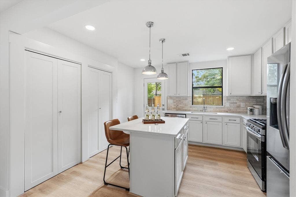 11624 Rupley Lane, Dallas, TX 75218 Kitchen featuring white shaker-style cabinetry, a central island with a solid-surface countertop, subway tile backsplash, stainless steel appliances, and wood-finish flooring