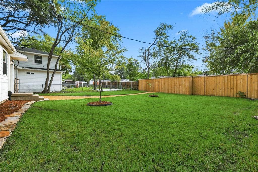 11624 Rupley Lane, Dallas, TX 75218 Backyard featuring a wood privacy fence, stone landscape edging, grass lawn, and gravel pathway