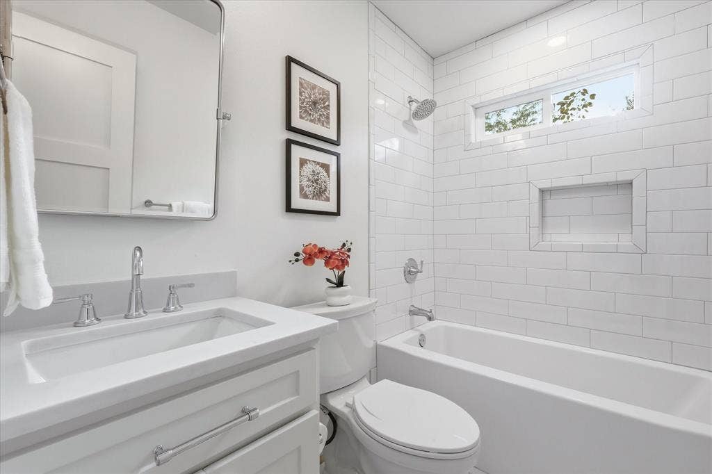 11624 Rupley Lane, Dallas, TX 75218 Bathroom featuring a white vanity with a composite countertop, rectangular undermount sink, white subway tile shower surround with a built-in recessed niche, and horizontal transom window