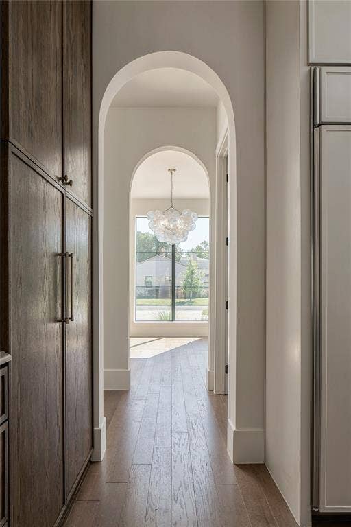 Arched architectural detail featuring floor-to-ceiling dark-stained cabinetry, wood-finish flooring, and a multi-light bubble chandelier
