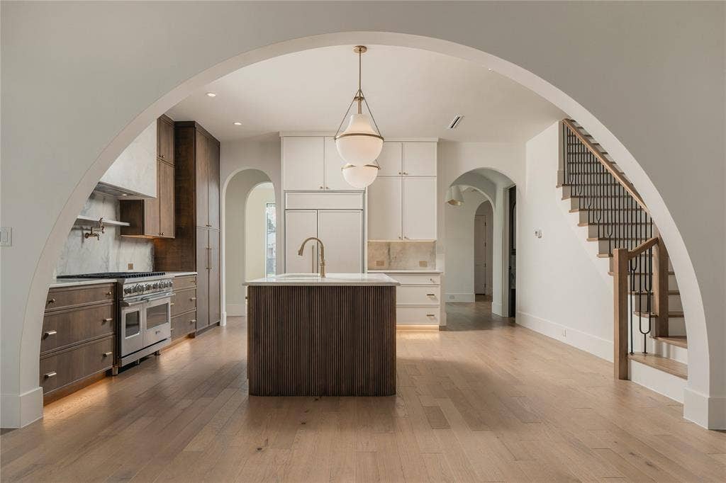 Kitchen featuring a large central island, custom dual-tone cabinetry, professional-grade range, wood-finish flooring, and a prominent arched entryway