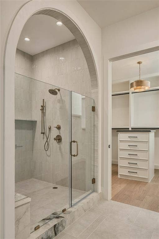 Walk-in shower featuring an arched entry, glass enclosure, stone-tiled floor, and brass-finish fixtures, complemented by a built-in chest of drawers with an integrated countertop
