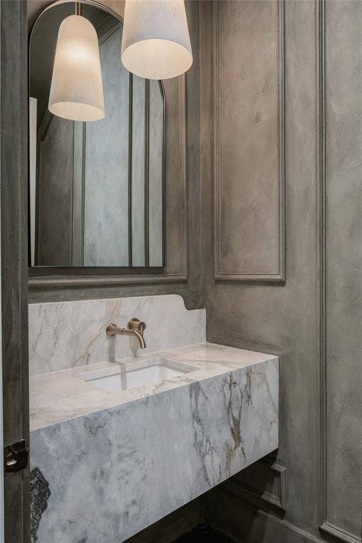 Floating vanity featuring stone slab construction, undermount sink, wall-mounted metallic faucet, arched mirror, and decorative wall molding