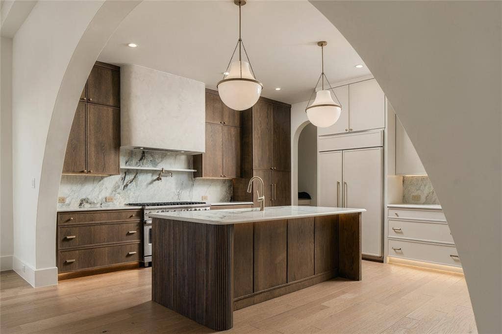Kitchen featuring arched architectural detailing, wood-finish cabinetry, a central island with integrated storage, stone-surfaced countertops, and pendant lighting