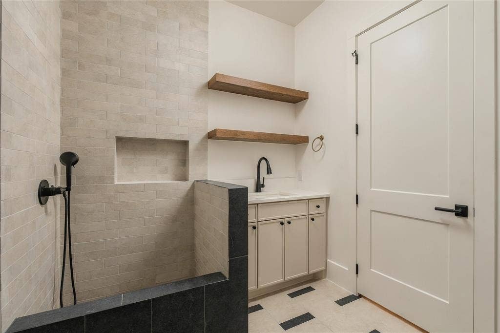 Custom cabinetry vanity with an undermount sink and matte black faucet, Dog Wash featuring a built-in wall niche and matte black handheld showerhead, natural stone-finish floor tiling, and wood-finish floating shelving