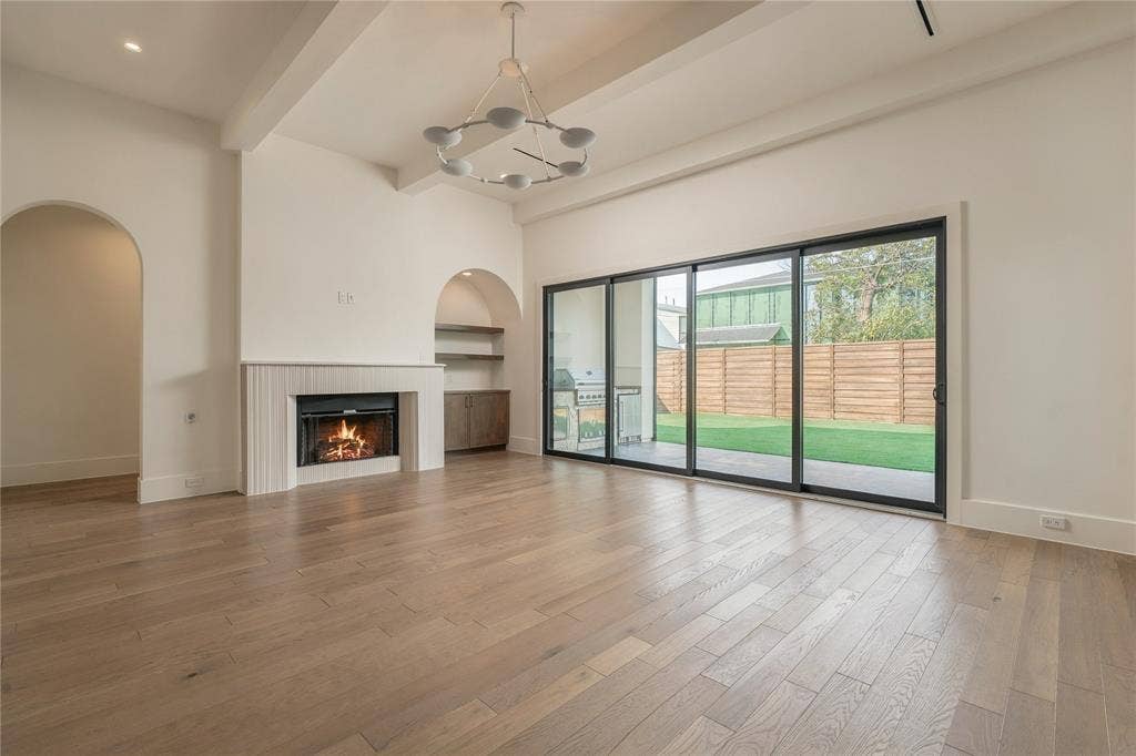 Living area featuring wood-finish flooring, vaulted ceiling with exposed beams, fireplace with fluted surround, built-in arched shelving, and oversized multi-panel sliding glass doors