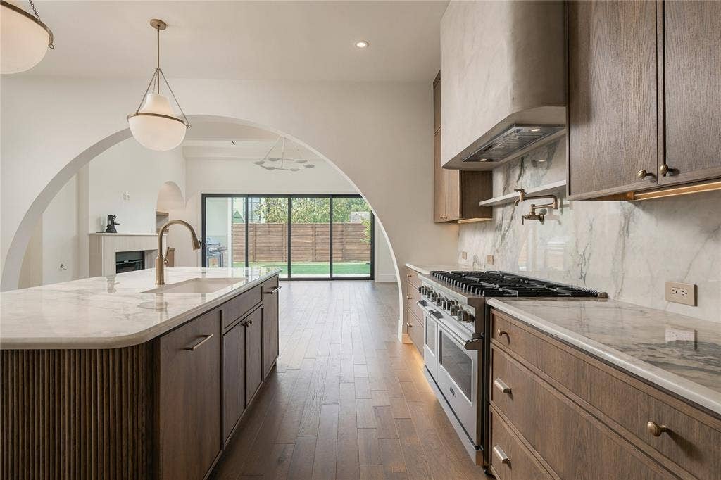 Kitchen featuring wood cabinetry, stone countertops, a professional-style range with a custom hood, and an expansive center island with a prep sink