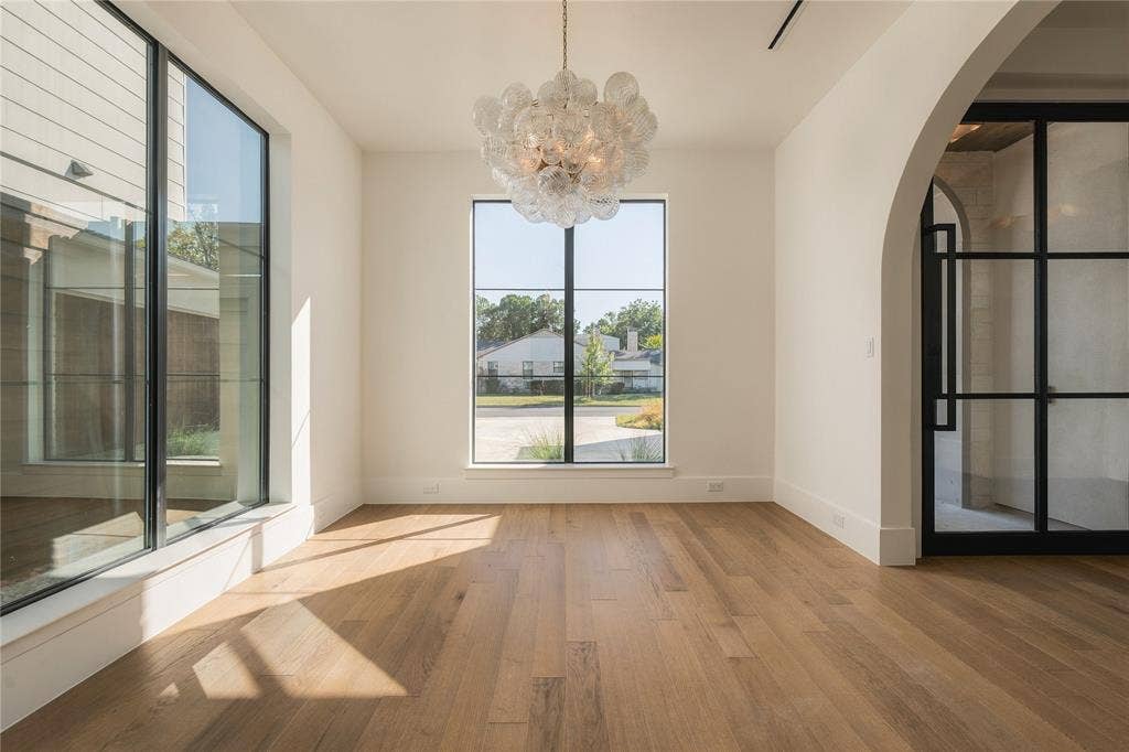 Interior space featuring wood-finish flooring, large multi-pane windows with black frames, a sculptural glass chandelier, and an arched entryway with a black-framed glass door
