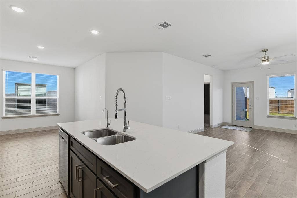 3125 Lucia Way, Princeton, TX 75407 Kitchen island featuring a stone-composite countertop, dual-basin stainless steel sink, gooseneck faucet, dark-finish shaker cabinetry, and wood-finish flooring