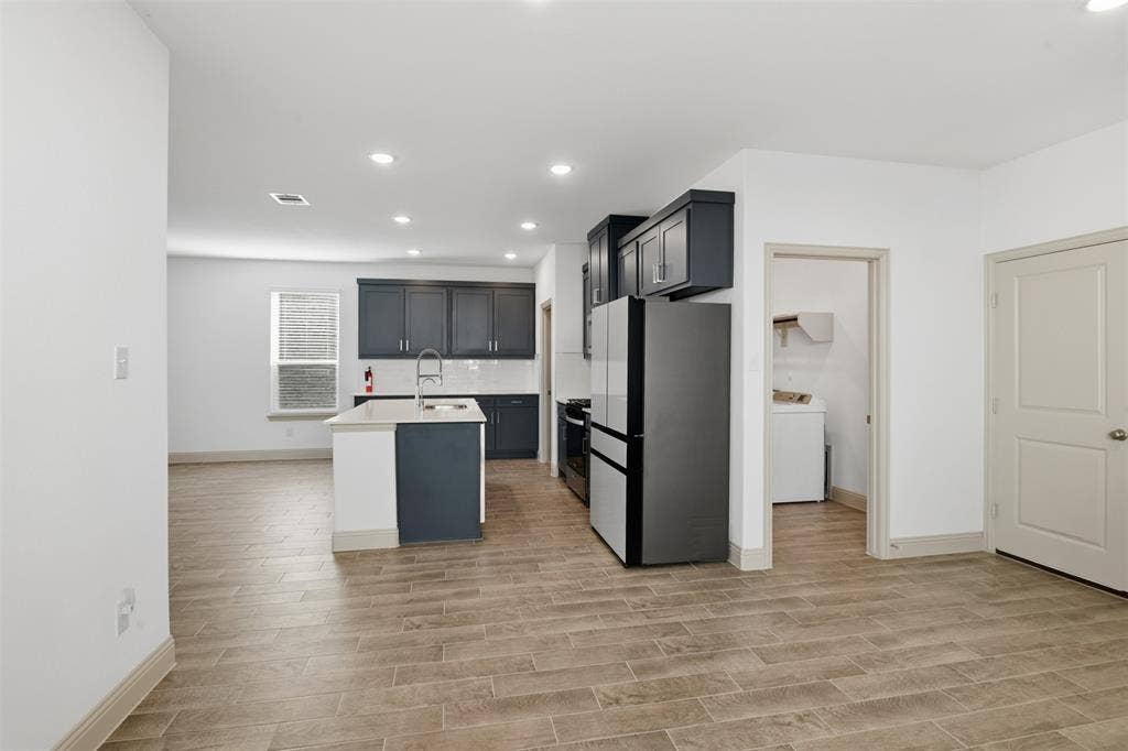 3125 Lucia Way, Princeton, TX 75407 Kitchen featuring dark cabinetry, center island with an integrated sink, neutral stone-finish countertops, wood-finish flooring, and recessed ceiling lighting