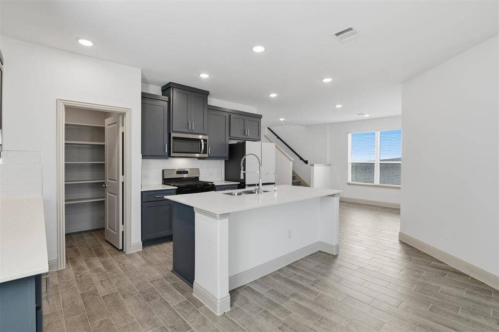 3125 Lucia Way, Princeton, TX 75407 Kitchen featuring dark cabinetry, solid-surface countertops, center island with undermount sink, built-in stainless steel microwave, and wood-finish tile flooring