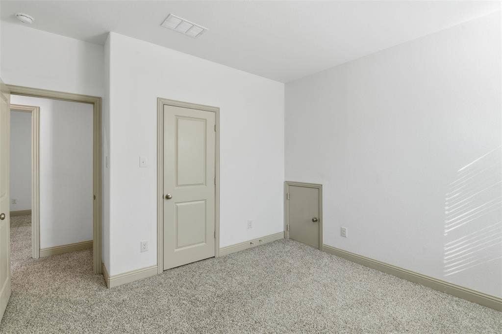 3125 Lucia Way, Princeton, TX 75407 Neutral interior space featuring textured wall-to-wall carpeting, crisp white walls, neutral-toned interior doors, and a built-in under-stair storage access door