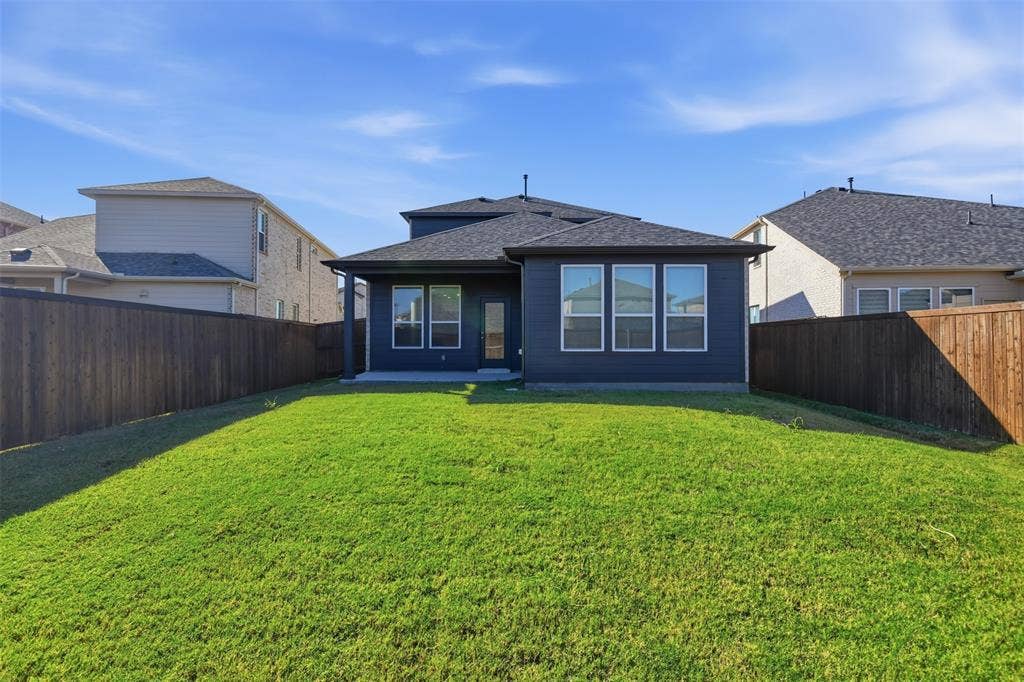 3125 Lucia Way, Princeton, TX 75407 Fenced backyard featuring a manicured lawn, dark-toned exterior siding, multiple rectangular windows, and a covered rear patio