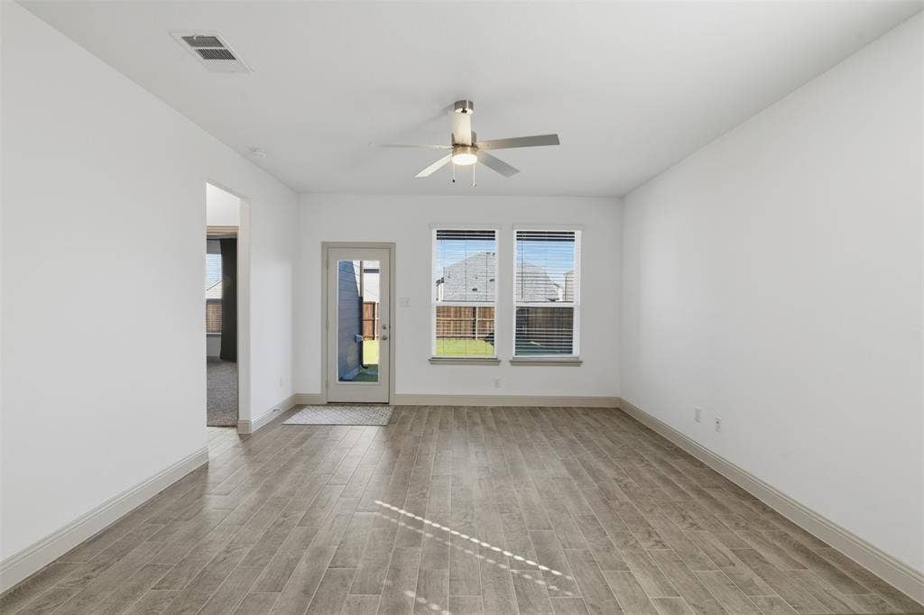 3125 Lucia Way, Princeton, TX 75407 Neutral-toned interior space featuring wood-finish flooring, dual windows, a central ceiling fan with integrated lighting, and a glass-paneled exterior door