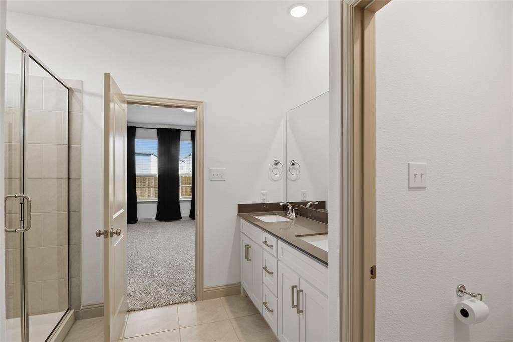 3125 Lucia Way, Princeton, TX 75407 Bathroom featuring a dual-sink vanity with a solid-surface countertop, glass-enclosed shower with tile surround, and tile flooring