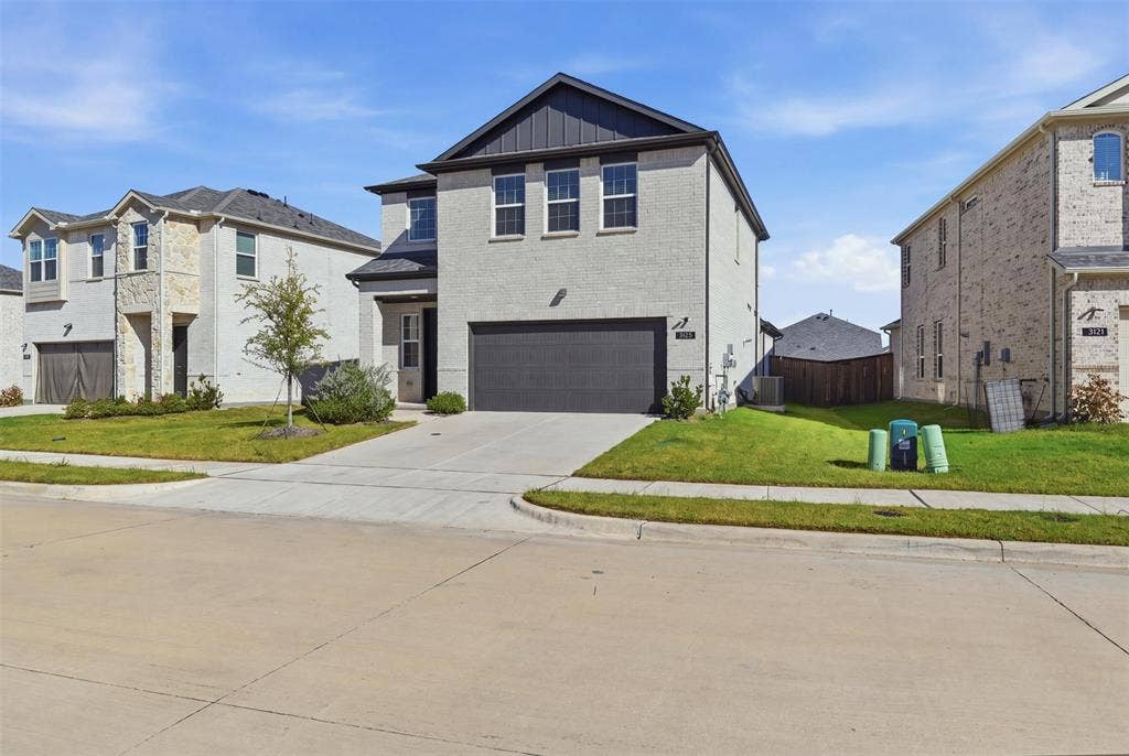 3125 Lucia Way, Princeton, TX 75407 Two-story residence featuring light-toned brick facade, dark-toned vertical siding accents, a front-facing attached two-car garage, and a concrete driveway