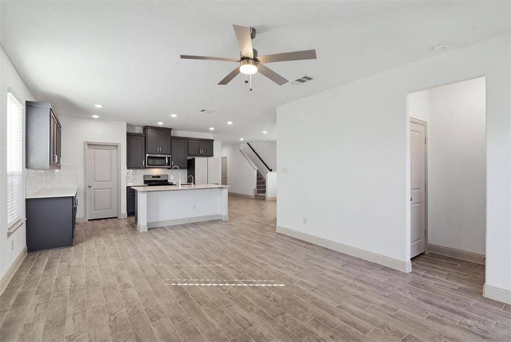 3125 Lucia Way, Princeton, TX 75407 Open-concept interior featuring wood-finish tile flooring, recessed lighting, a modern ceiling fan, dark cabinetry, and a kitchen island with a stone-finish countertop