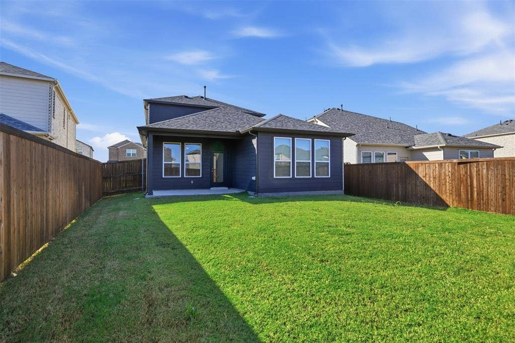 3125 Lucia Way, Princeton, TX 75407 Rear exterior featuring dark-toned horizontal siding, a concrete patio, a private fenced yard, and multiple windows with white trim
