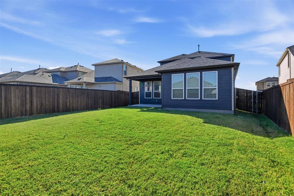 3125 Lucia Way, Princeton, TX 75407 Expansive backyard featuring a sod lawn, horizontal wood-plank fencing, covered concrete patio, dark-toned siding, and energy-efficient windows