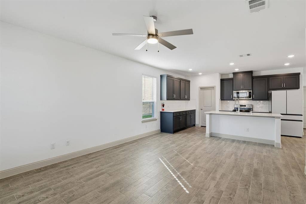 3125 Lucia Way, Princeton, TX 75407 Open-concept kitchen featuring dark-finish cabinetry, a white countertop island with an integrated sink, wood-finish flooring, recessed lighting, and a modern ceiling fan