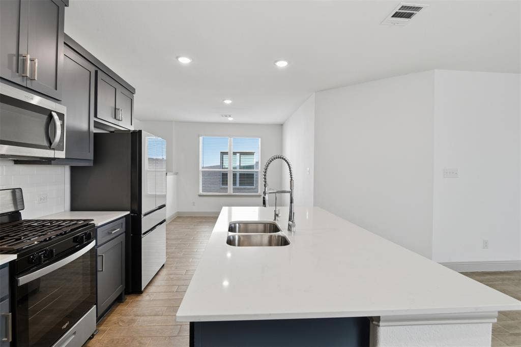 3125 Lucia Way, Princeton, TX 75407 Kitchen featuring shaker-style cabinetry, quartz countertops, a dual-basin stainless steel sink with a high-arch faucet, and wood-finish flooring