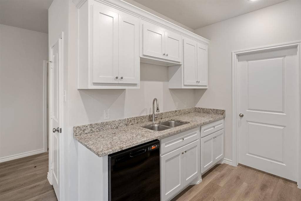 6144 Shawnee Drive, Mabank, TX 75156 White shaker-style cabinetry, stone-finish countertops, stainless steel dual-basin sink with arched faucet, black built-in dishwasher, and wood-finish flooring