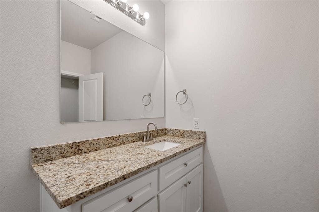 6144 Shawnee Drive, Mabank, TX 75156 White vanity cabinetry featuring an integrated stone countertop, undermount rectangular sink, polished chrome faucet, and large wall-mounted mirror with multi-bulb light fixture