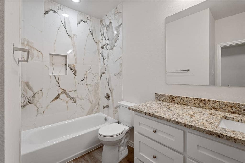 6144 Shawnee Drive, Mabank, TX 75156 Bathroom featuring full-height stone-patterned wall tile, built-in shower niche, vanity with stone-finished countertop, undermount sink, and white cabinetry