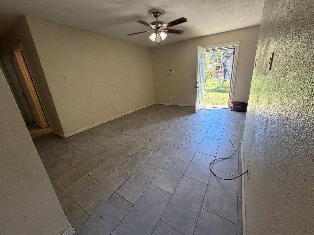 Interior space featuring large-format tile flooring, a ceiling fan with integrated lighting, and a single-pane glass-panel exterior door