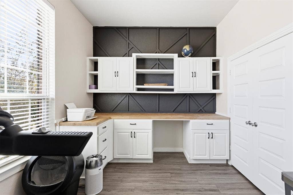 Built-in desk area with white cabinetry, wood-finish countertop, geometric wall accent, and wood-finish flooring