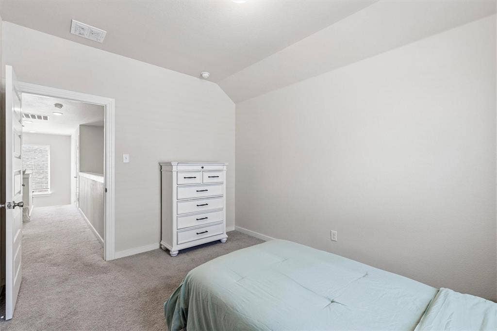 Neutral-toned room featuring a vaulted ceiling and wall-to-wall carpeting