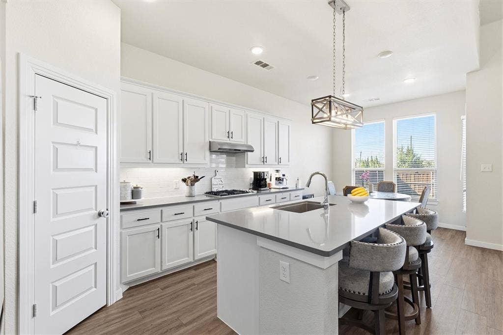Kitchen featuring white cabinetry, solid-surface countertops, center island with integrated sink, stainless steel range hood, and wood-finish flooring
