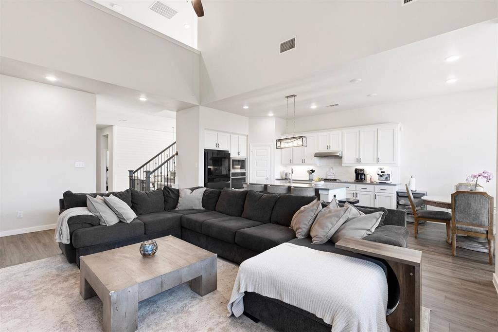 Open-concept interior featuring vaulted ceilings, recessed lighting, white cabinetry, a center island with pendant lighting, and wood-finish flooring