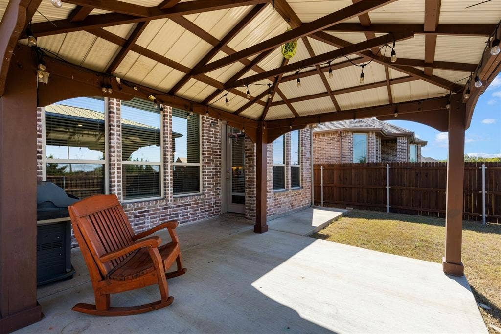 Covered patio featuring a timber-frame pergola, concrete flooring, brick exterior siding, and a fenced rear yard